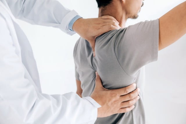 A provider examines a patient's shoulder with his hands