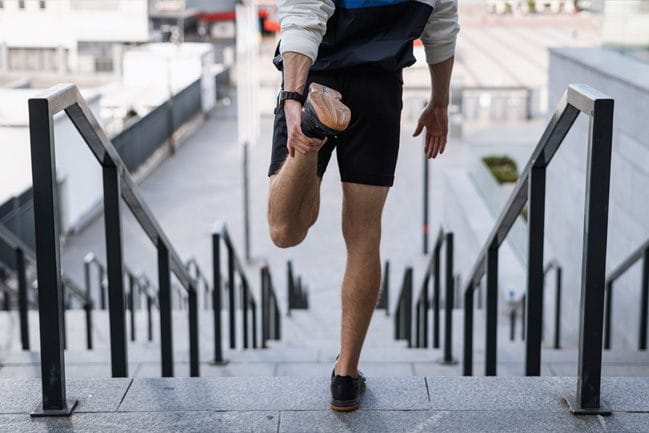 Male athlete stretching quads and ankle on steps