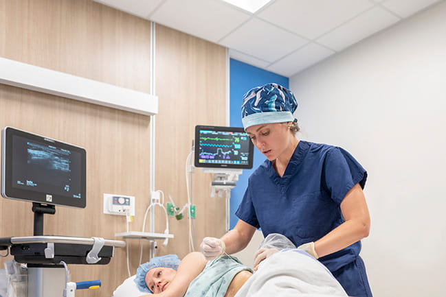 Physician inserting needle into lower torso of a resting patient