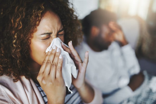 Woman sneezing into a tissue.