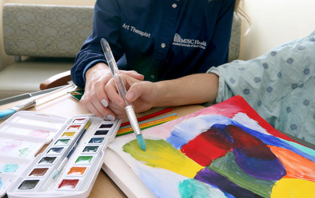 MUSC Arts in Healing art therapist with hospital patient at the bedside painting colorful images in art therapy session