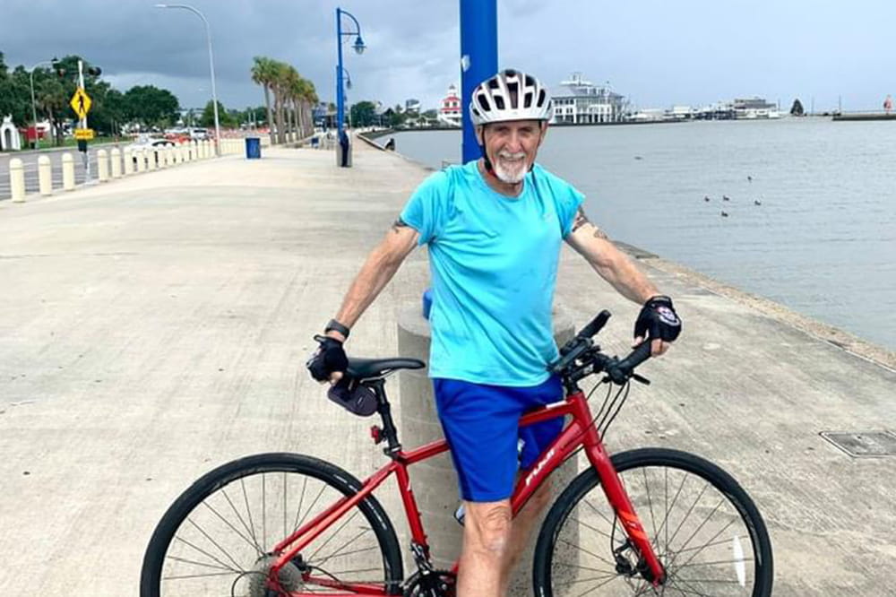 a man poses on his bike on a wide paved area parallel to water