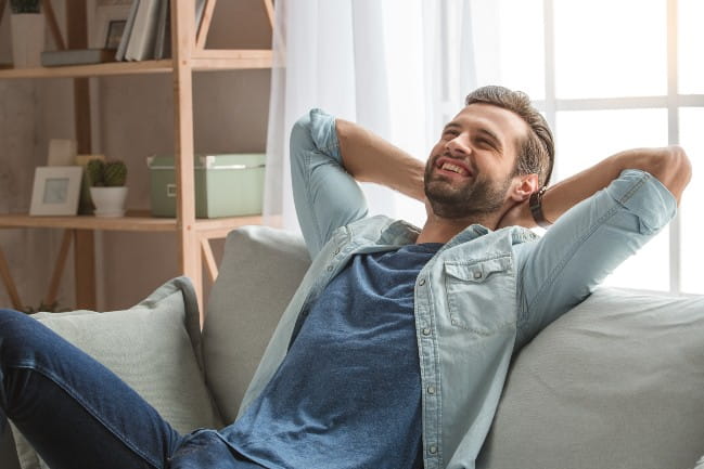 Decorative image of relaxed, smiling man on couch with arms locked behind his head.