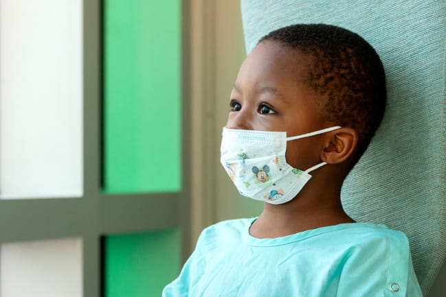 A four-year-old boy in a light blue hospital gown wears a mickey mouse mask at MUSC.  