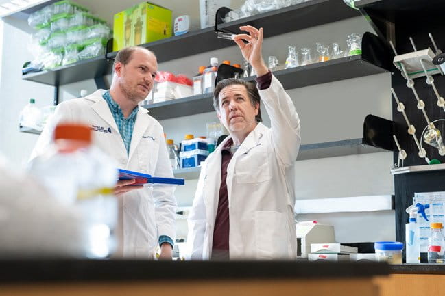 Two scientists in a laboratory examine a microscope slide