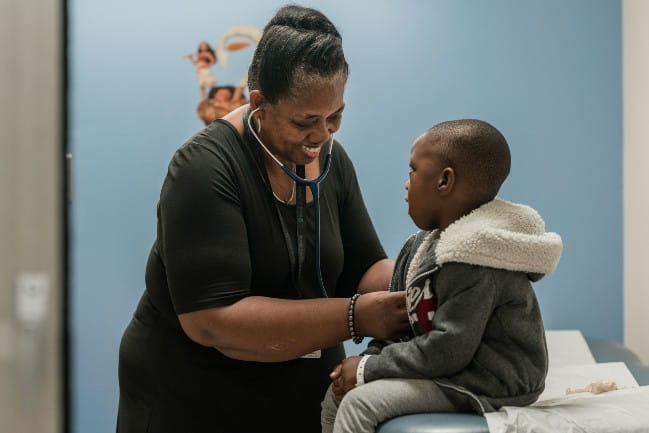 Smiling care team member listening to child's heartbeat using a stethascope.