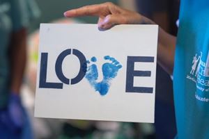 Volunteer holding craft project with the print of baby feet on it and letters that spell LOVE.