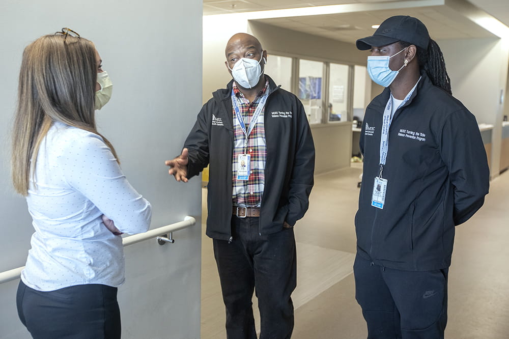 three people stand in a hospital hallway chatting