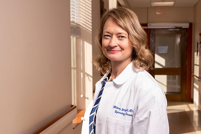 a woman wearing a white doctor's coat stands in a hallway